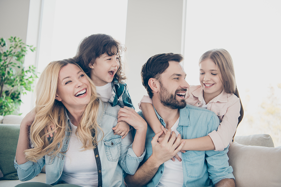 Mother, father, and two daughters hugging and laughing on a couch | ACA Marketplace Plans