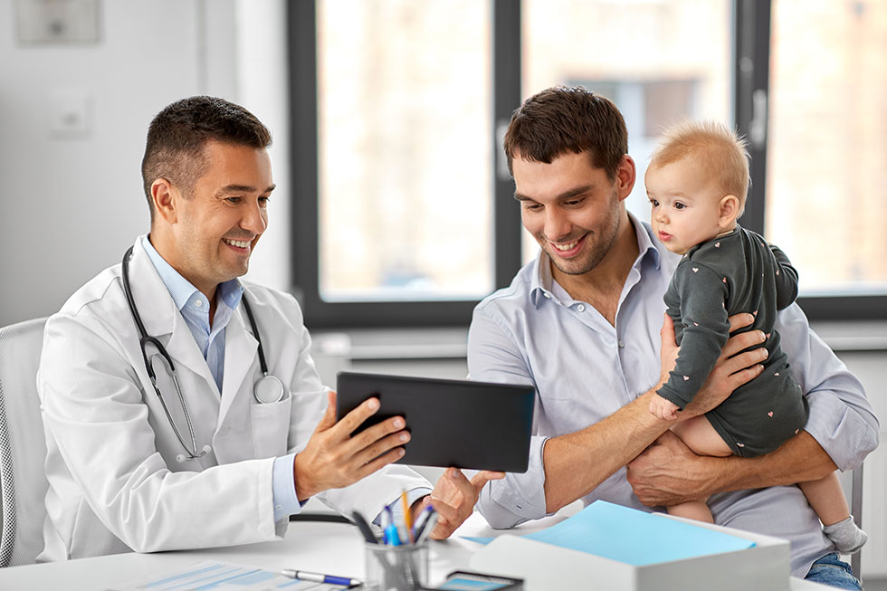 A father with his son in his arms taking to his doctor.